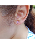 Close-up of a woman wearing a pink sapphire stud earring with blurred background.