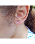 Close-up of a woman wearing a pink sapphire stud earring with blurred background.