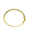 The lateral side profile view of a gold bangle bracelet with emeralds on a white background.
