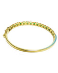 A yellow gold bangle bracelet with round cut emeralds on a underside view position.