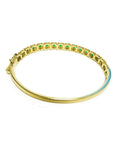 A yellow gold bangle bracelet with round cut emeralds on a underside view position.