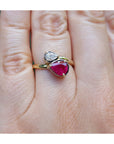 A natural ruby and diamond you and me ring made of 18k yellow gold, shown worn on a person's finger.