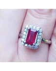 Emerald-cut ruby ring with diamond halo, set in 14K white gold on a finger.