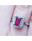 Emerald-cut ruby ring with diamond halo, set in 14K white gold on a finger.