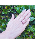 Women's 14K white gold ring with an emerald-cut deep red ruby and diamond halo on a hand.