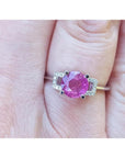 Round cut pinkish-red Mozambique ruby ring with accented diamonds in 14k white gold on a finger.
