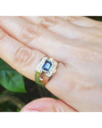 Gold ring with a blue sapphire gemstone on a finger against a blurred green background