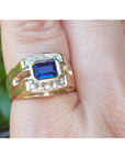 Gold ring with a blue natural sapphire and diamonds on a finger against a blurred background