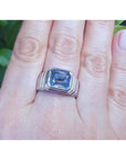 Men's 18K white gold ring with a bezel-set, emerald-cut vivid blue sapphire on a hand.