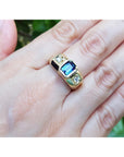 Gold ring with a blue sapphire gemstone on a hand against a blurred green background