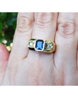 Gold ring with a blue natural sapphire gemstone on a hand against a blurred green background