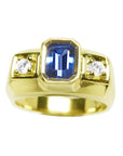 Men’s natural sapphire ring featuring an emerald-cut vibrant medium blue stone in a bezel setting, accented by side round-cut diamonds, crafted in 14K yellow gold.