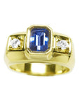 Men’s natural sapphire ring featuring an emerald-cut vibrant medium blue stone in a bezel setting, accented by side round-cut diamonds, crafted in 14K yellow gold.