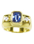 Men’s natural sapphire ring featuring an emerald-cut vibrant medium blue stone in a bezel setting, accented by side round-cut diamonds, crafted in 14K yellow gold.