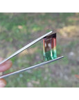 Fancy cut 8.30 carat Brazilian Watermelon Tourmaline gemstone, vibrant red-orange and bluish-green, held in tweezers.