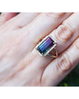 Ring with a colorful tourmaline gemstone on a hand against a blurred natural background