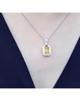 Emerald cut yellow sapphire halo diamond pendant on an 18K white gold chain, worn on a woman.