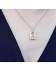 Emerald cut yellow sapphire halo diamond pendant on an 18K white gold chain, worn on a woman.