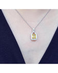 Emerald cut yellow sapphire halo diamond pendant on an 18K white gold chain, worn on a woman.