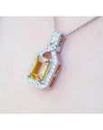 Emerald cut yellow sapphire pendant with halo diamonds on an 18K white gold chain, worn on a woman's neck.