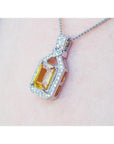 Emerald cut yellow sapphire pendant with halo diamonds on an 18K white gold chain, worn on a woman's neck.