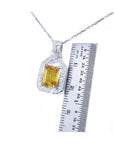 Emerald cut yellow sapphire pendant with diamond halo on an 18K white gold chain, shown with a ruler.