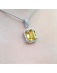 Emerald cut yellow sapphire pendant with diamond halo on an 18K white gold chain.