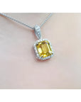 Emerald cut yellow sapphire pendant with diamond halo on an 18K white gold chain.
