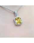 Emerald cut yellow sapphire pendant with diamond halo on an 18K white gold chain.