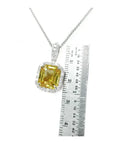 6.01 ct. emerald cut yellow sapphire pendant with diamond halo in 18K white gold, next to a ruler.