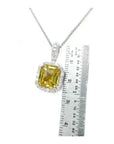 6.01 ct. emerald cut yellow sapphire pendant with diamond halo in 18K white gold, next to a ruler.