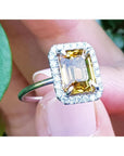 Emerald cut 4.59 ct yellow sapphire halo diamond ring in 14K white gold, worn on a finger.