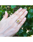 Hand wearing a white gold ring with a yellow natural yellow sapphire against a green leafy background