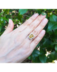 Emerald cut 4.59 ct yellow sapphire ring with diamond halo in 14K white gold on a hand.