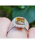 Emerald cut yellow sapphire ring with diamond halo in 14K white gold on a finger.
