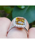 Emerald cut yellow sapphire ring with diamond halo in 14K white gold on a finger.