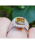 Emerald cut yellow sapphire ring with diamond halo in 14K white gold on a finger.
