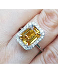 14k white gold Ring with a yellow natural sapphire emerald cut and diamond accents on a finger.