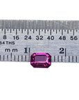 Vibrant, deep reddish-pink, emerald-cut natural ruby next to a ruler for size reference.