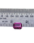 Vibrant, deep reddish-pink, emerald-cut natural ruby next to a ruler for size reference.