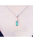 A woman wearing an emerald and diamond briolette necklace in 14k white gold with a natural diamond