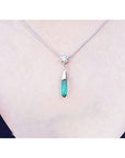 A woman wearing an emerald and diamond briolette necklace in 14k white gold with a natural diamond
