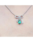 18K white gold bow-tie necklace with pear-shaped emerald and diamonds on a chain.