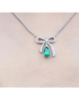 18K white gold bow-tie necklace with pear-shaped emerald and diamonds on a chain.