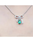 18K white gold bow-tie necklace with pear-shaped emerald and diamonds on a chain.