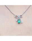 18K white gold bow-tie necklace with pear-shaped emerald and diamonds on a chain.