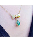 18K yellow gold bow-tie necklace with pave diamonds and a dangling pear-shaped emerald.