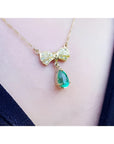 18K yellow gold bow-tie necklace with pave diamonds and a dangling pear-shaped emerald.