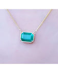 Emerald-cut Colombian emerald solitaire necklace in 18K yellow gold, worn on a person.