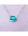 Emerald-cut Colombian emerald solitaire necklace in 18K yellow gold, worn on a person.